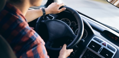 A person holding the steering wheel and driving a car.