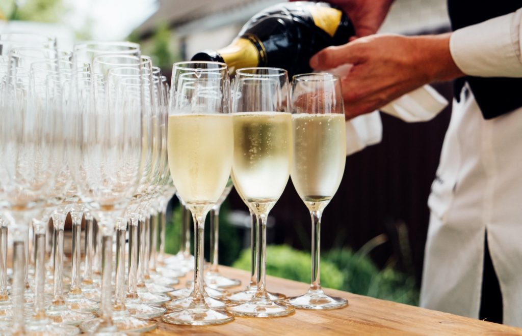 Wedding bartender pours champagne into crystal glasses for guests.