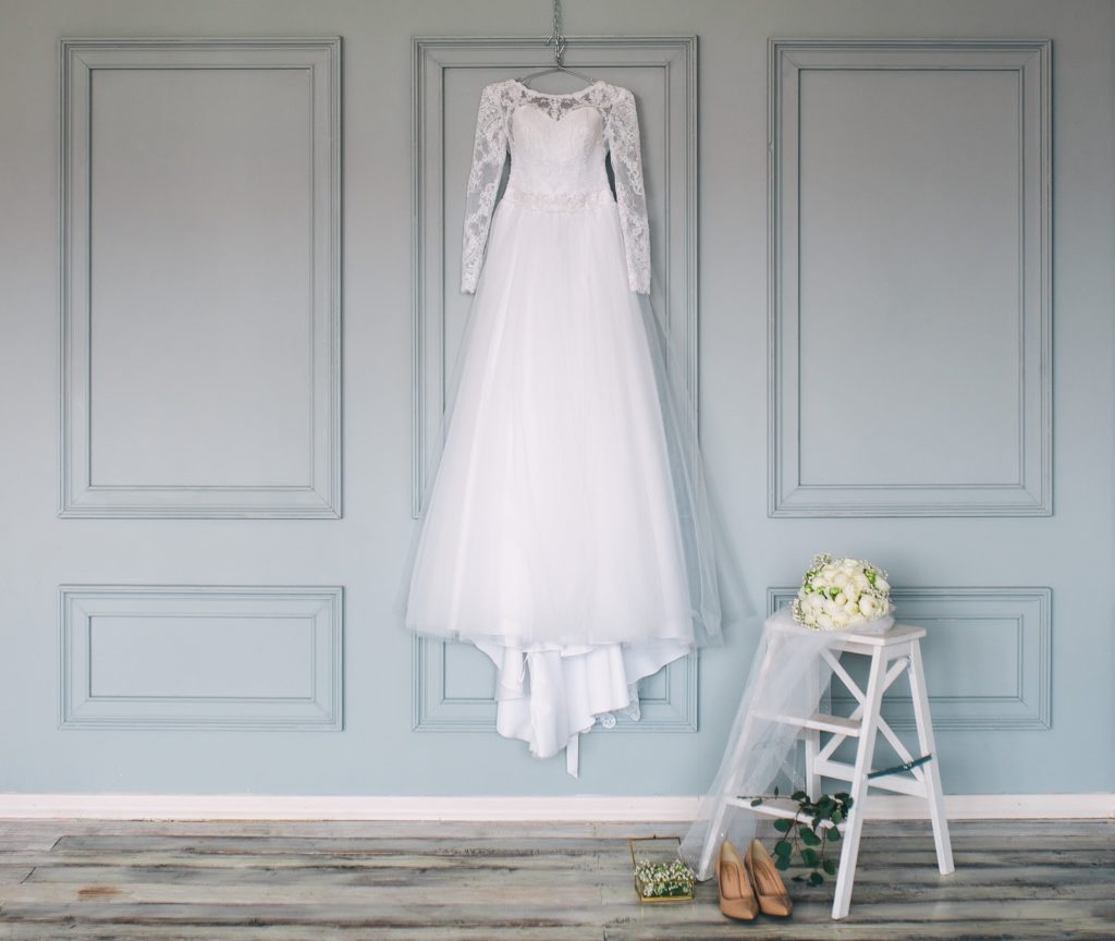 Wedding dress hangs on wall with other accessories nearby.