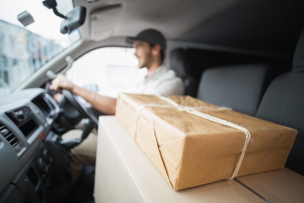 A delivery driver is driving a van with brown paper packages in the front seat.