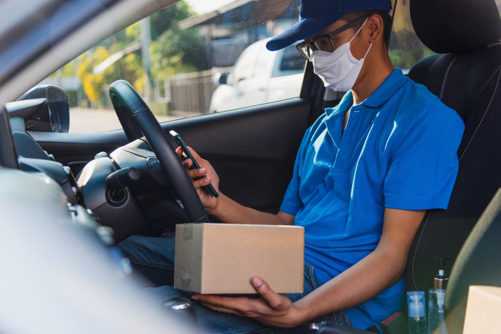 A delivery driver checks an order on his phone with the package in his hand during a daytime delivery.