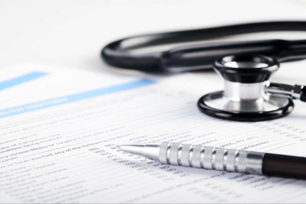 A close-up picture of a stethoscope and a pen lying on top of a health insurance document.