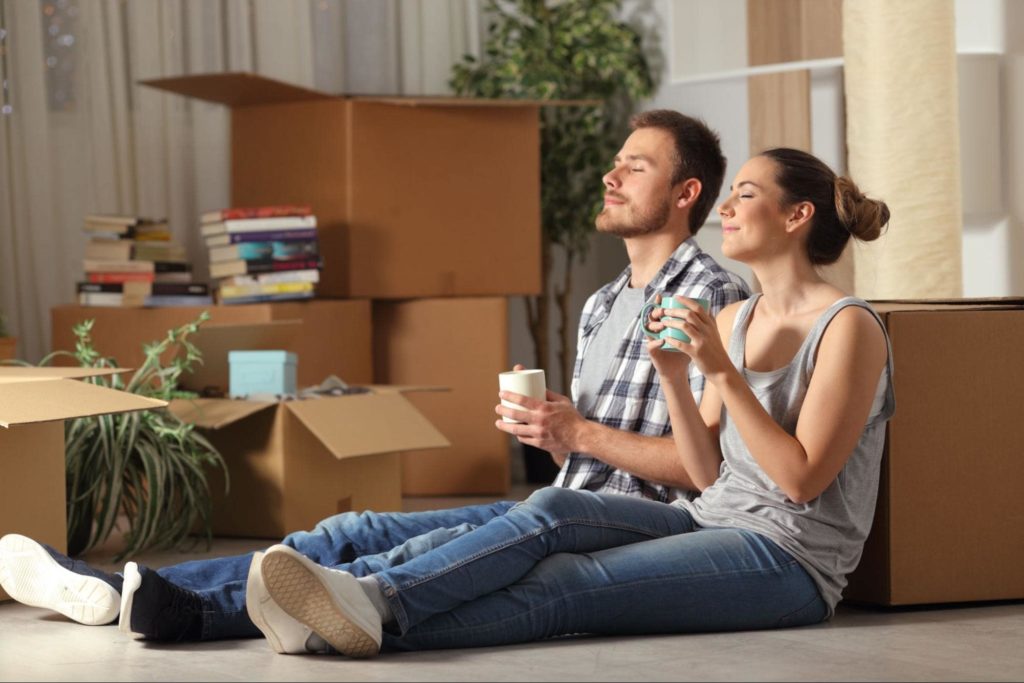 A picture of a young couple leaning against a cardboard box enjoying a cup of coffee and relaxing after moving.