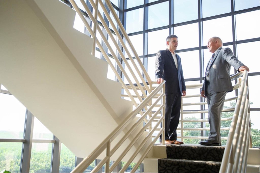 Two business men speaking at the top of the stairs.