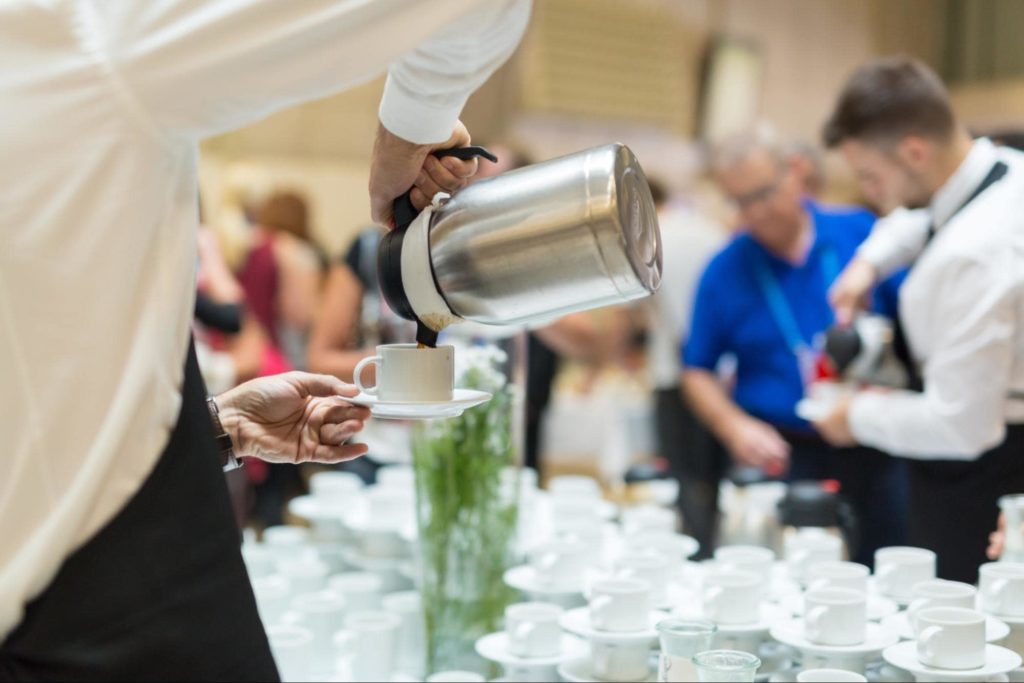 A catering employee pouring coffee at a fancy event.