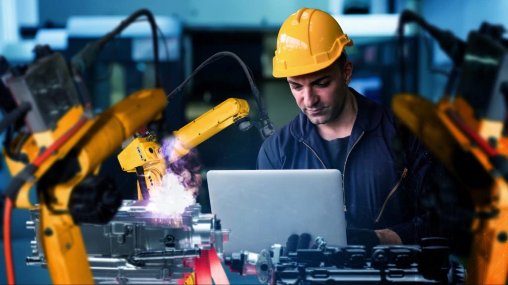 A manufacturing worker looking down at a laptop while surrounded by equipment.