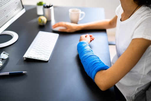 A woman with a broken arm sitting at her desk working at a computer.