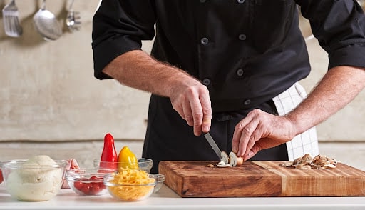 A private chef chopping mushrooms on a cutting board. They are covered by private chef insurance. 
